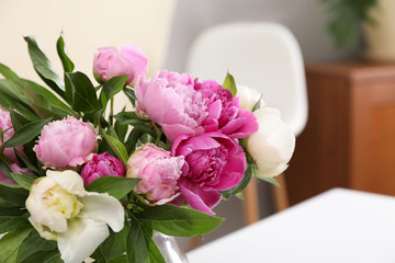 Bouquet of beautiful peonies on table in room, closeup. Space for text