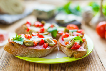 Traditional Italian bruschetta with blue cheese, feta, tomatoes, basil leaves, jamon on a wooden background.