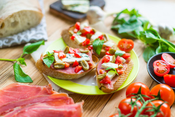 Traditional Italian bruschetta with blue cheese, feta, tomatoes, basil leaves, jamon on a wooden background.