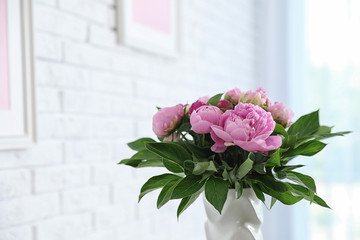 Vase with bouquet of beautiful peonies at white wall in room, space for text