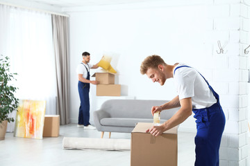 Fototapeta na wymiar Moving service employee sealing cardboard box with adhesive tape in room