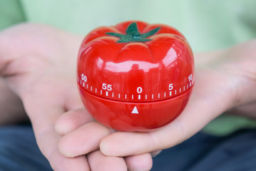 Red tomato kitchen timer set to 0, held by both hands, with open palms