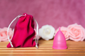 Pink sack bag and menstrual cup from medicinal silicone. Pink and white roses. Concept of zero waste alternative for popular intimate hygiene products for period.