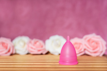 Pink menstrual cup from a medicinal silicone. Pink and white roses decoration. Concept of eco friendly alternative and zero waste solution of intimate hygiene.