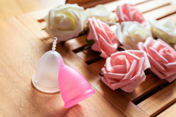 Top view of menstrual cups from a medicinal silicone. Decoration from pink and white roses. Concept of take care of woman body and health. Zero waste.