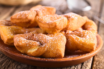 Traditional Chilean sweet calzones rotos deep-fried pastries sprinkled with powdered sugar served on wooden plate (Selective Focus, Focus on the front of the first pastry)