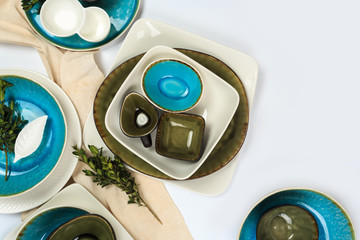 Simple rustic handmade blue and green crockery against white wooden wall: dish, stack of bowls.  Top view