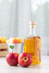 Healthy organic food. Apple cider vinegar or juice in glass bottle and fresh red apples on a light background.