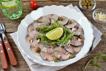 Fresh mackerel carpaccio with capers, parmesan, arugula and olive oil on an old wooden background.