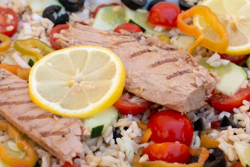 Rice salad with fresh vegetables and grilled mackerel decorated with a slice of lemon