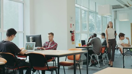 Serious girl coming in coworking space. Young men working in open space.