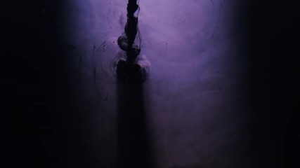 Dark ink injected into violet water from top. Liquid dye infusion. Ocean contamination.