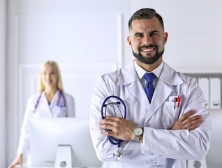 Handsome smiling male doctor. Welcome to our clinic. Confident physician. Office background. Man practitioner with a stethoscope. Successful medic. Friendly staff. Copy space for your text.