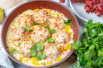 CRABMEATBALLS crab meatballs in white creamy sauce in red pan, whole king crab, cilantro, lemon and white wine on white background