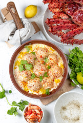 CRABMEATBALLS crab meatballs in white creamy sauce in red pan, whole king crab, cilantro, lemon and white wine on white background