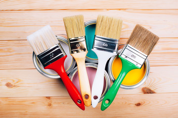 Four open cans of paint with brushes on them on wooden natural background.