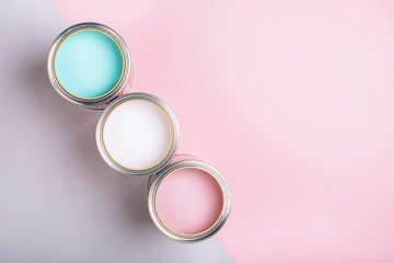 Three open cans of pastel paint on pink and grey background.