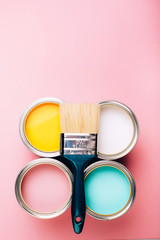 Brush with green handle on open cans on pink pastel background.