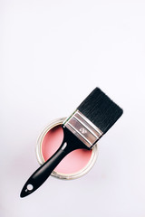 Brush with black handle on open can of pink paint on grey background.