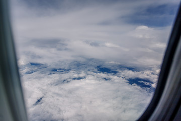 Plane window view with blue sky and beautiful clouds. As seen through window of an aircraft. View of wing & ocean. Airplane from city Bangkok to island Bali.