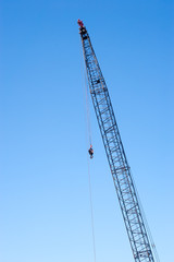 Tall industrial crane with hook on clear blue sky.