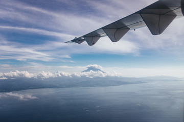 Plane window view with blue sky and beautiful clouds, sky. As seen through window of an aircraft. View of wing, ocean, volcano Agung & Nusa Penida. Airplane from island Bali to Labuan Bajo, Komodo.