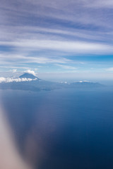 Plane window view with blue sky and beautiful clouds. Clouds and sky as seen through window of an aircraft. View of ocean and volcano Agung. Airplane from island Bali to Labuan Bajo, Komodo.