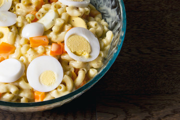 Serving bowl of macaroni salad topped with eggs and orange peppers; a hearty home made macaroni salad served fresh
