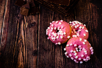 Aged wooden table with delicious pink donuts for lunch tasty sweets for young people, copy space.