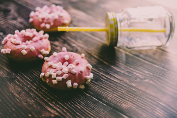 Pair of buns frosted with pink sugar and unhealthy marshsmallows next to a glass jar.