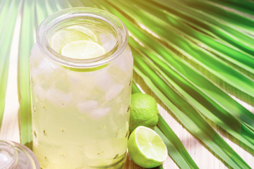 Cold fresh lemonade drink with lime slice and ice cubes in a jar on a tropical background