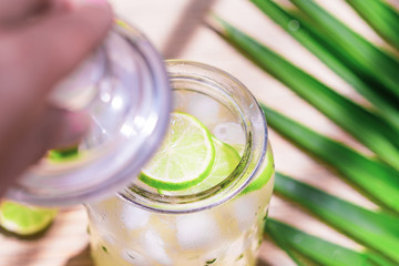 Cold fresh lemonade drink with lime slice and ice cubes in a jar on a tropical background