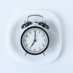 Alarm clock on the white plate. Time to eat, Breakfast, Lunch time and dinner concept. Black and White Concept