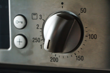 A close-up of a metal temperature and mode switch on the oven indicates a temperature of 180 degrees, selective focus