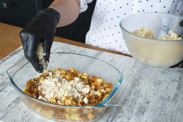 Womens black-gloved hands make apple crisp pie, put dough crumbs on grated apple