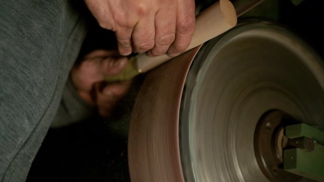 SLOW MOTION, CLOSE UP: Unrecognizable craftsman sandpapering a small piece of wood into a knife handle. Sawdust comes flying off block of wood being made into a handle by the experienced craftsman.