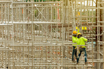 asian construction workers working on scaffolding of building construction site in city. urban...