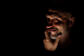  Face with a bearded man grimace against a dark background with sharp shadows. Comedic, fabulous villain or negative character conception with copy space.