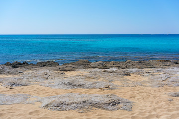 Sandy Mediterranean Sea beach with flat rocks on, Greece.
