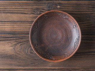 Clay bowl on a brown wooden table. The view from the top. Pottery for the kitchen.