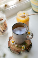 Healthy chamomile tea in a teacup and honey on white windowsill background, remedy alternative concept
