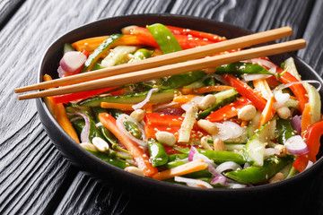 Salad of cucumbers, peppers, carrots, pea pods with sesame and peanuts close-up on a plate. horizontal