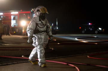 firefighters in silver suit operating on airport site at night. 