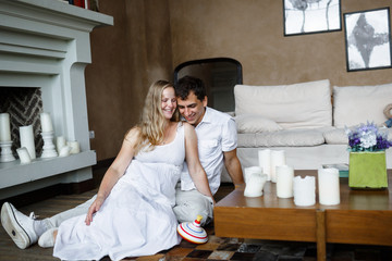 Lovely young happy couple sits on a floor hugging and laughing, girl is pregnant