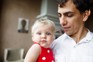 Portrait of happy father and 1 years old blonde daughter in red dress at home