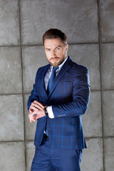 Young handsome business man, fashion blue suit with tie, hairstyle, beard, watch. 