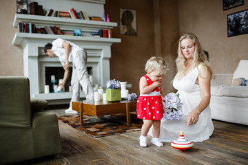 Pregnant woman in white dress playing with one year old baby sitting on a floor