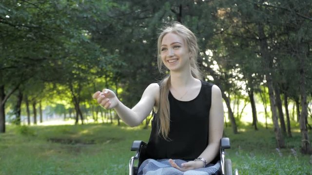 Beautiful blonde girl is sitting in wheelchair and having fun by playing and throwing frisbee