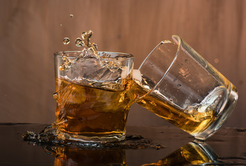Two glasses of whiskey with ice hit and break, pouring a lot of spray and drops