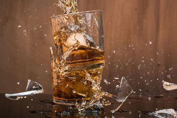 Two glasses of whiskey with ice hit and break, pouring a lot of spray and drops